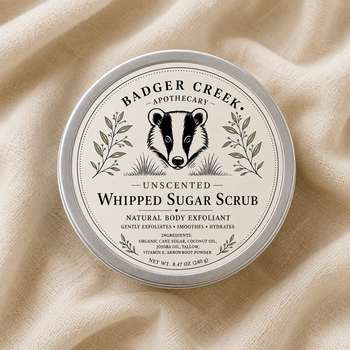 A round container of Badger Creek Apothecary Unscented Whipped Sugar Scrub, featuring a cream-colored label with a black badger illustration and green botanical details, set against a textured beige linen background.
